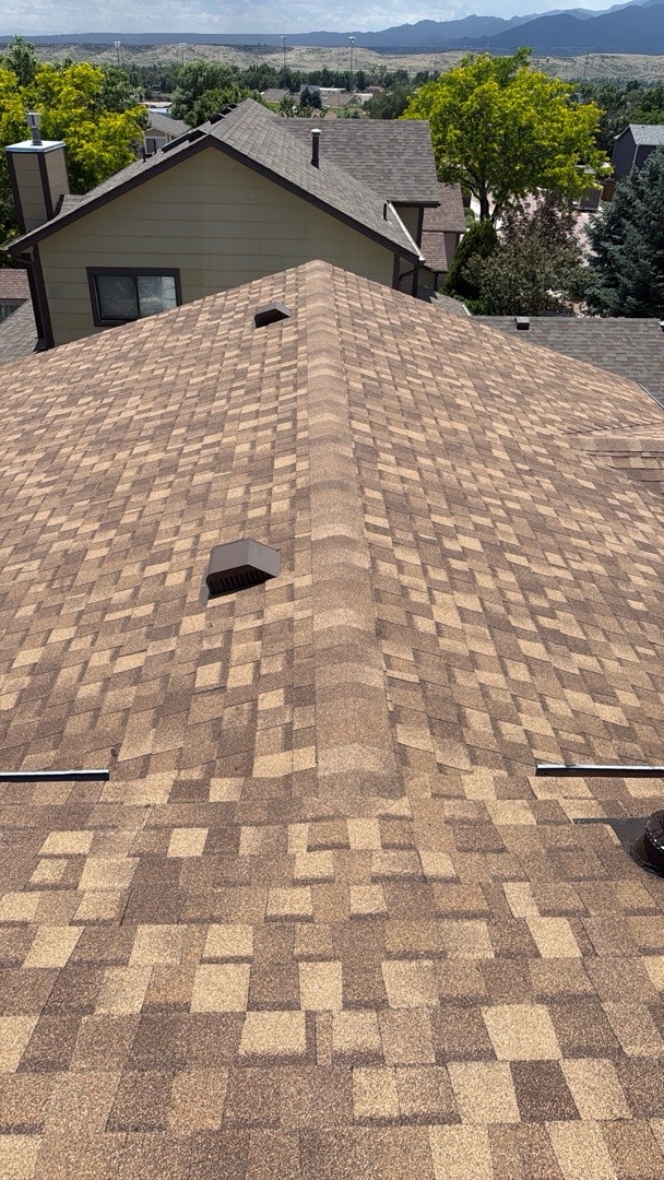 Completed weathered-wood shingle roof with slope-mounted attic vents and Front Range mountain views in Security-Widefield, CO